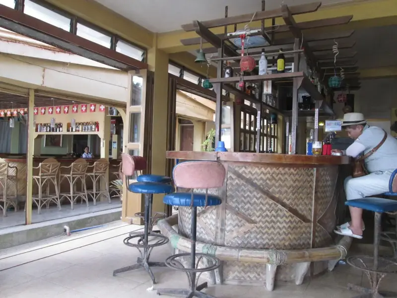 Un comptoir de bar en bois est entouré de tabourets hauts dans un espace lumineux et ouvert.