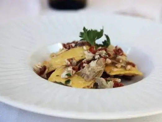 Assiette de raviolis au poulet et aux tomates cerises, décorée de persil frais.