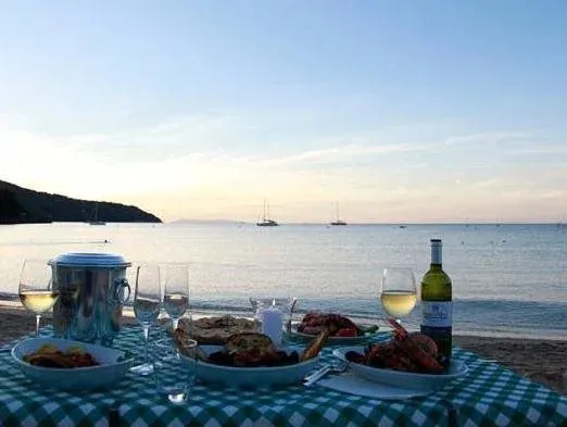 Une table dressée avec des plats et des boissons face à la mer au coucher du soleil.