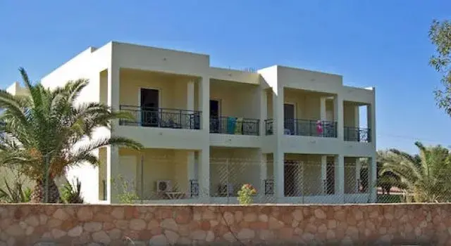 Bâtiment blanc à étages avec des balcons et des palmiers devant.