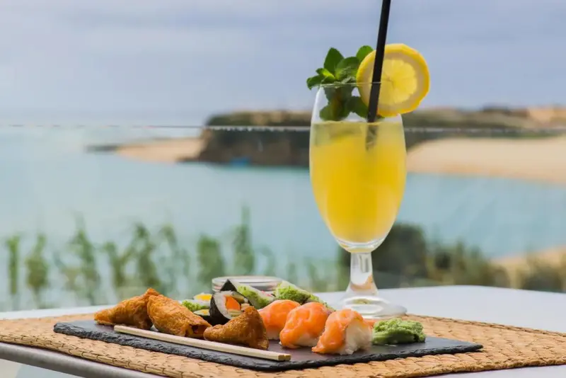 Un cocktail et des sushis sont servis sur une table en terrasse avec vue sur la mer.