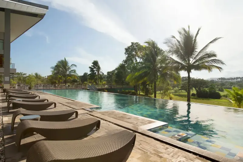Transats alignés au bord d'une piscine à débordement avec végétation luxuriante en arrière-plan.