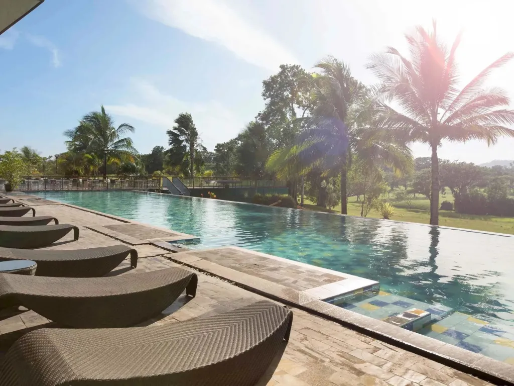Transats au bord d'une piscine à débordement avec végétation tropicale en arrière-plan.