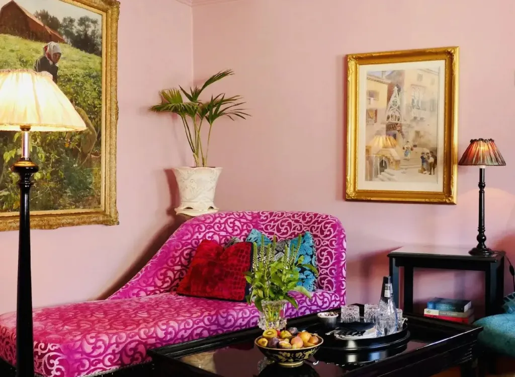 Un canapé rose et rouge est placé devant un mur rose, agrémenté de tableaux et de lampes.