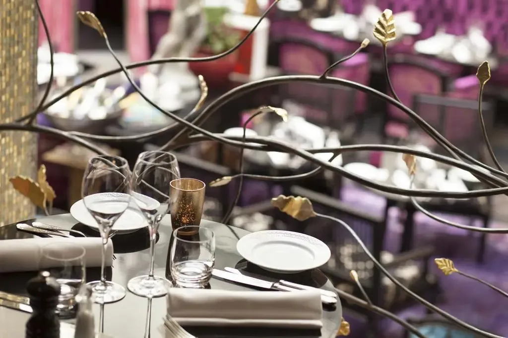 Une table est dressée avec de la vaisselle, des couverts et des verres dans une salle à manger décorée.