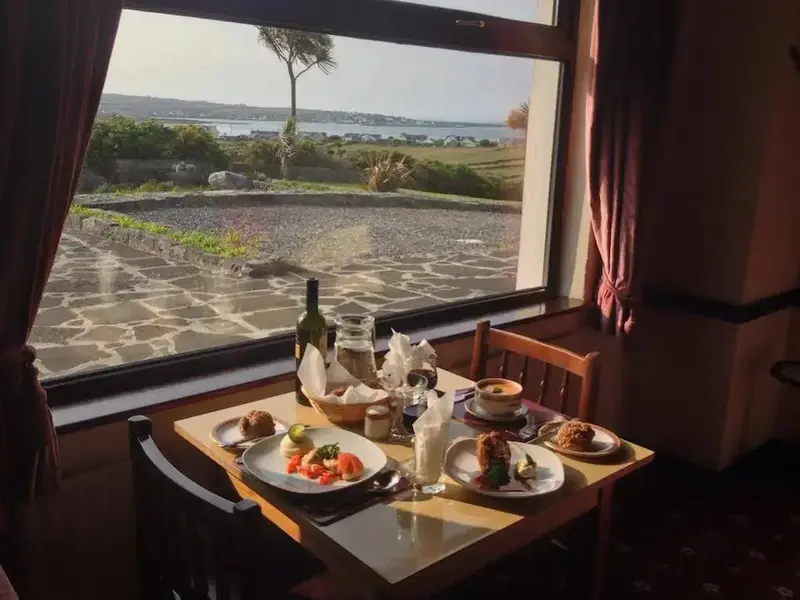 Une table est dressée devant une grande fenêtre donnant sur un paysage côtier.