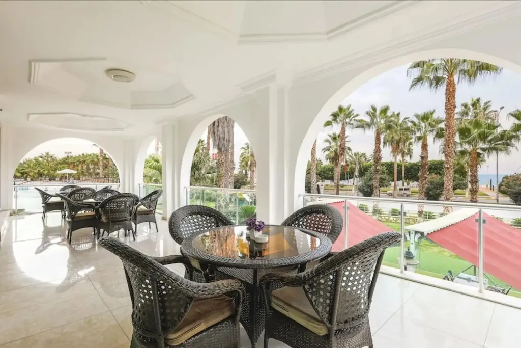 Terrasse ombragée avec tables et chaises donnant sur une végétation luxuriante et la mer.