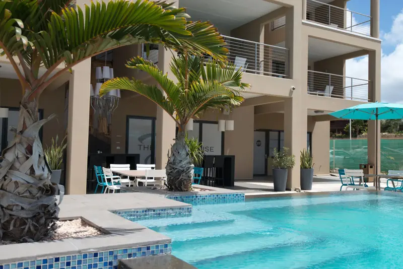Une piscine turquoise avec des marches et des chaises longues turquoise à proximité d'un bâtiment moderne.