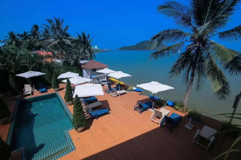 Terrasse en bois avec transats et parasols près d'une piscine et de la mer.
