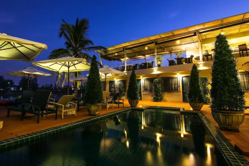 Piscine illuminée avec transats et végétation luxuriante au bord d'un bâtiment éclairé.