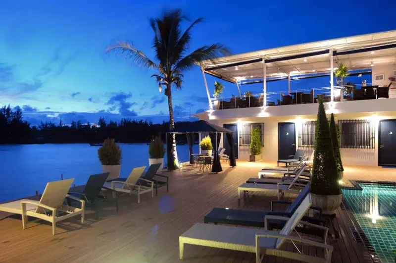 Terrasse lumineuse avec transats et végétation tropicale au bord de l'eau.