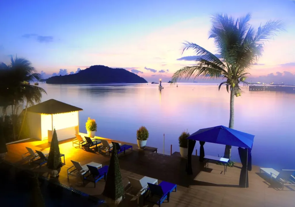 Terrasse aménagée avec transats et parasols face à la mer au coucher du soleil.