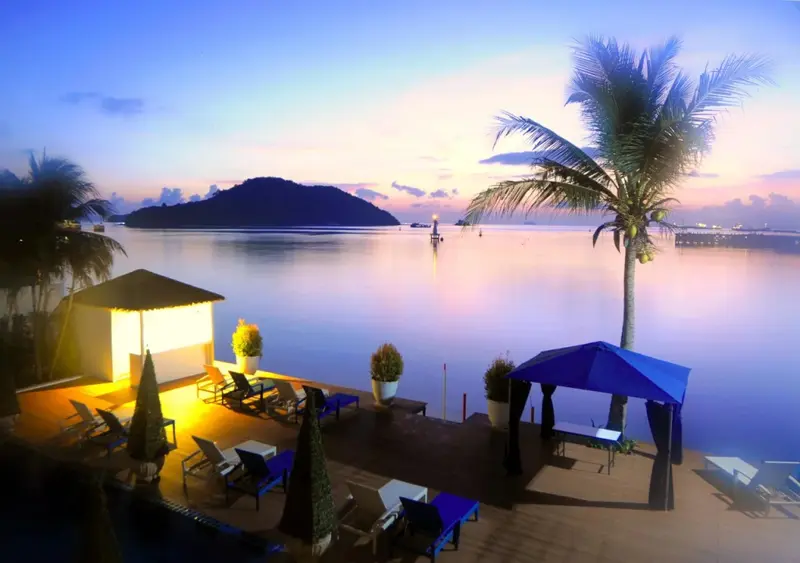 Terrasse aménagée avec transats et parasols face à la mer au coucher du soleil.