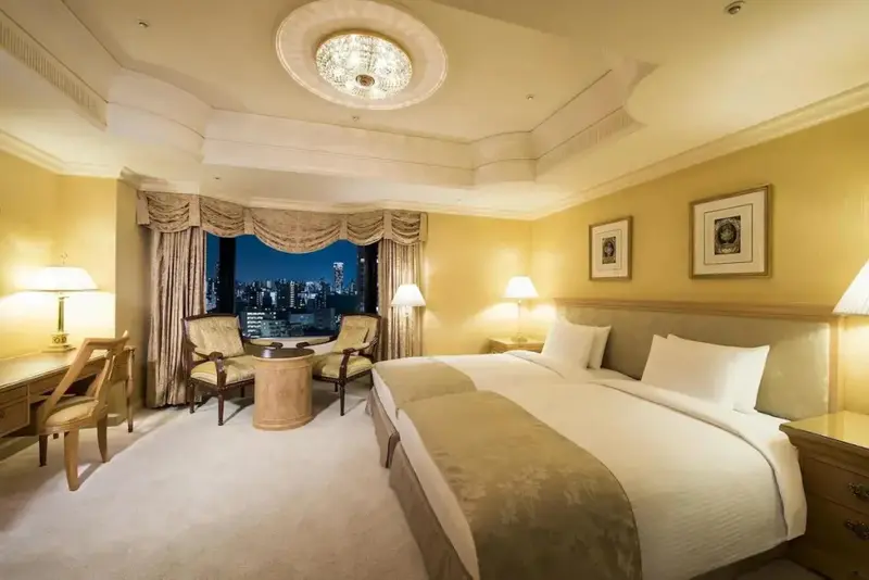 Chambre lumineuse avec un grand lit et un coin salon près d'une fenêtre.