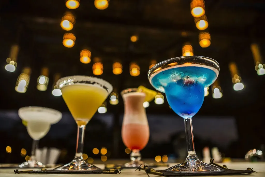 Des cocktails colorés sont servis sur une table éclairée par des guirlandes lumineuses.