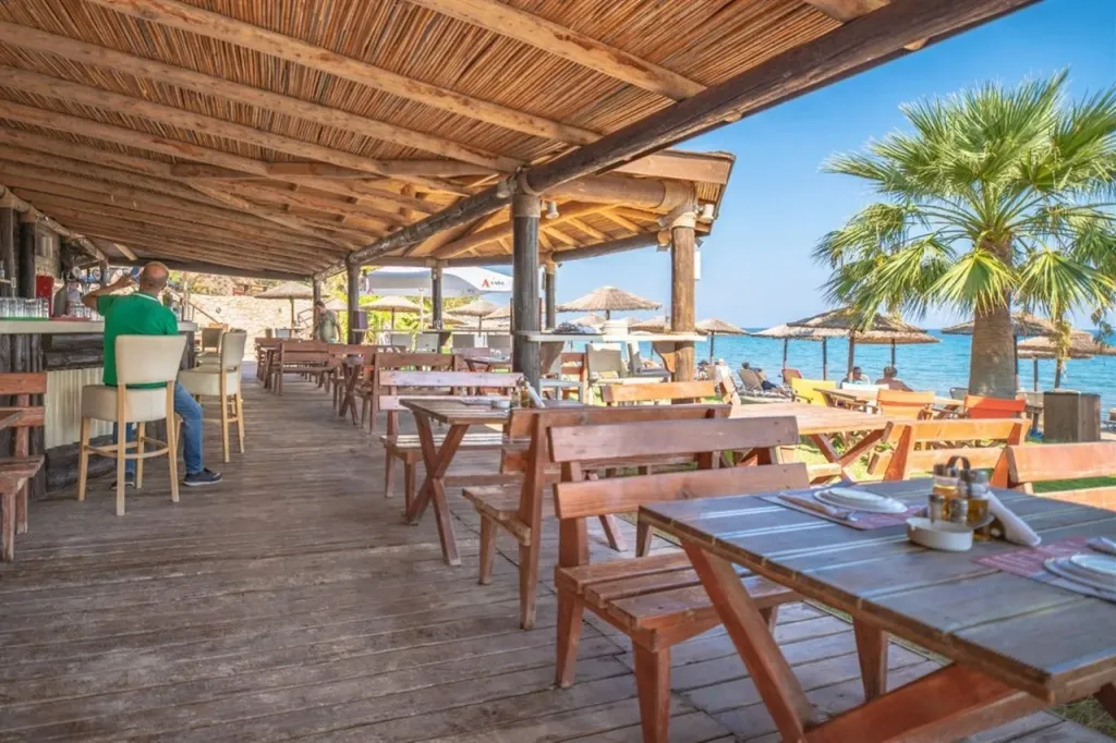 Terrasse de restaurant en bois avec tables et chaises face à la mer.