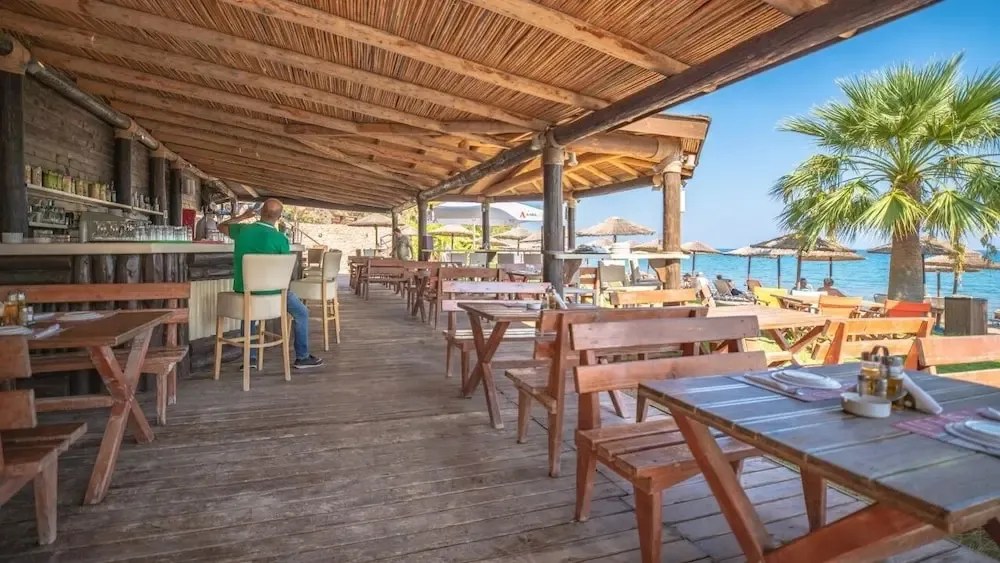 Terrasse de restaurant en bois avec tables et bar en bord de mer.