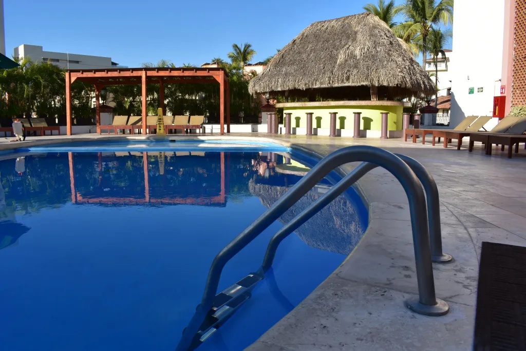 Une piscine rectangulaire avec un bar en fond et des transats sur le bord.