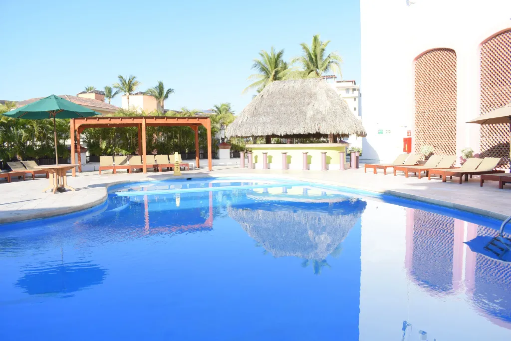 Une piscine rectangulaire avec un bar en fond et des transats.
