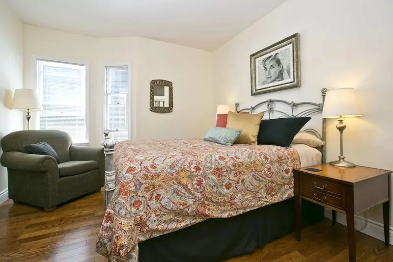 Une chambre lumineuse avec un lit recouvert d'une courtepointe colorée et un fauteuil.