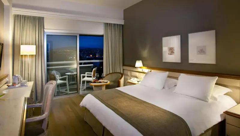 Une chambre lumineuse avec un grand lit et un balcon offrant une vue sur la ville.