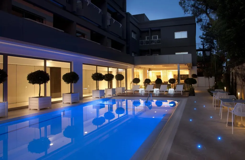 Piscine illuminée avec transats et tables à proximité d'un bâtiment.