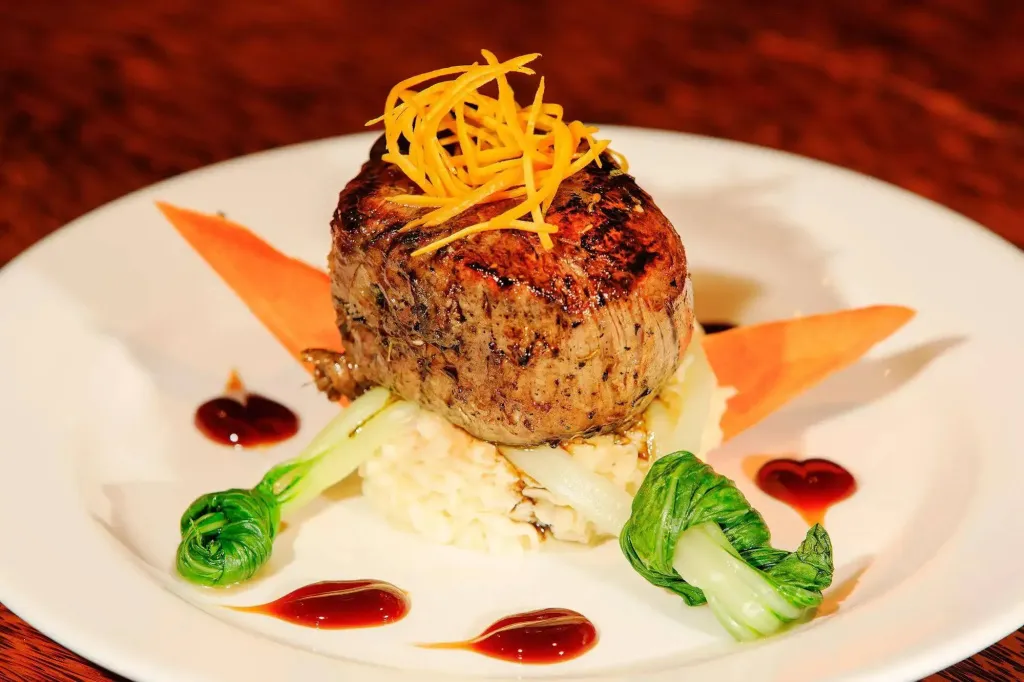 Une portion de viande grillée est présentée sur une assiette blanche avec une purée et des légumes.