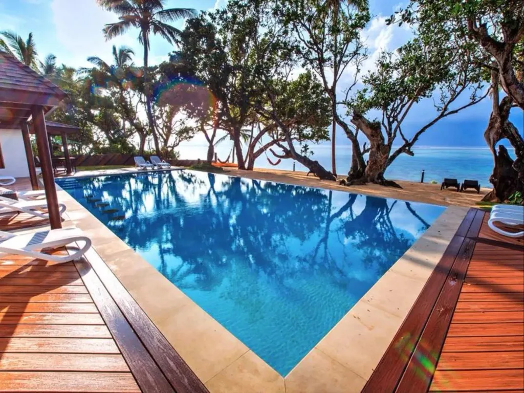 Une piscine rectangulaire bordée d'une terrasse en bois, avec des transats et une végétation luxuriante en arrière-plan.
