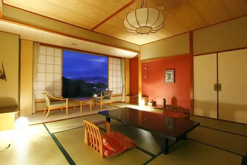 Une pièce lumineuse avec une table basse et des coussins sur des tatamis, donnant sur une vue nocturne.