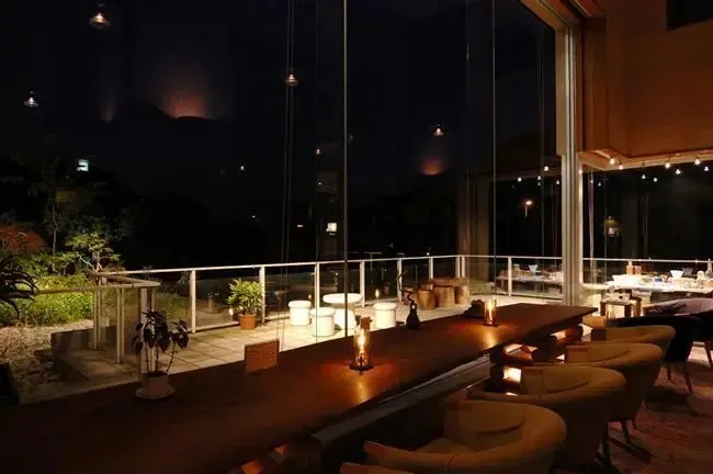 Terrasse lumineuse avec tables et chaises donnant sur une vue nocturne.