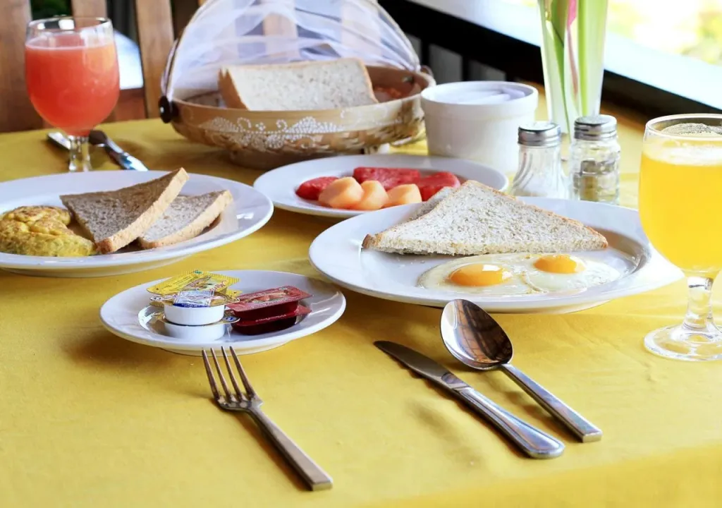 Une table est dressée avec un petit-déjeuner composé de fruits, d'œufs et de pain.