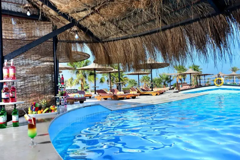 Une piscine bordée de transats sous des parasols de chaume.