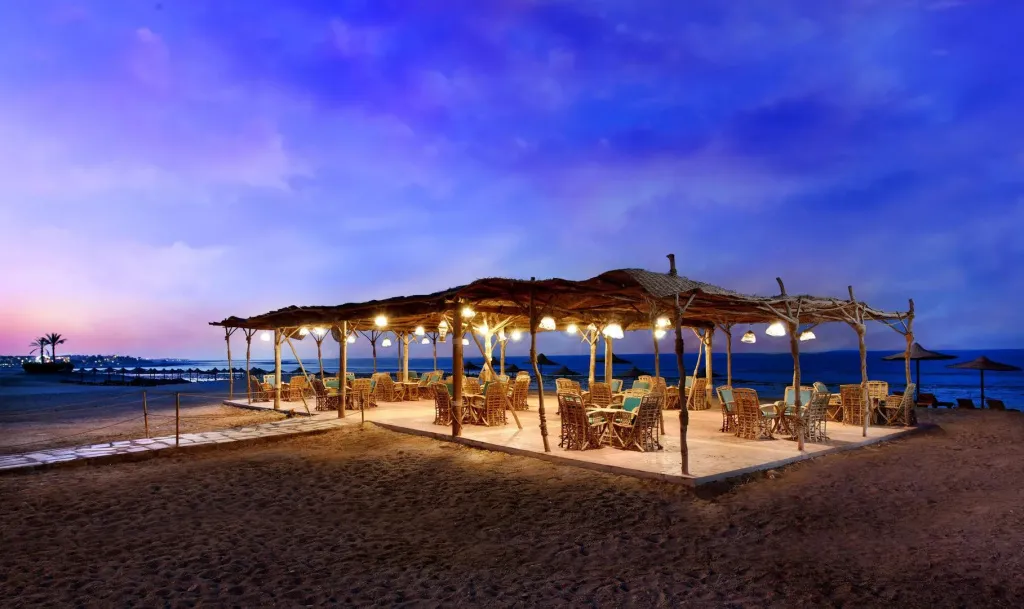 Terrasse de restaurant éclairée au crépuscule sur une plage de sable.