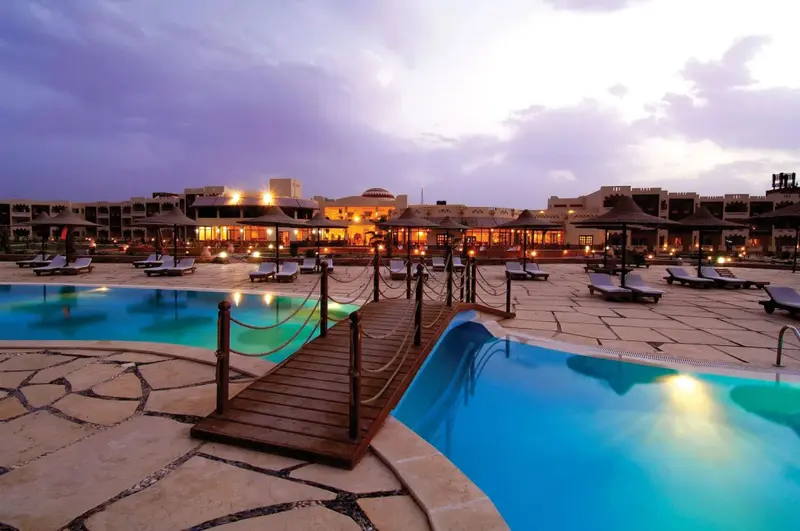 Plusieurs piscines s'étendent devant un bâtiment illuminé au crépuscule.