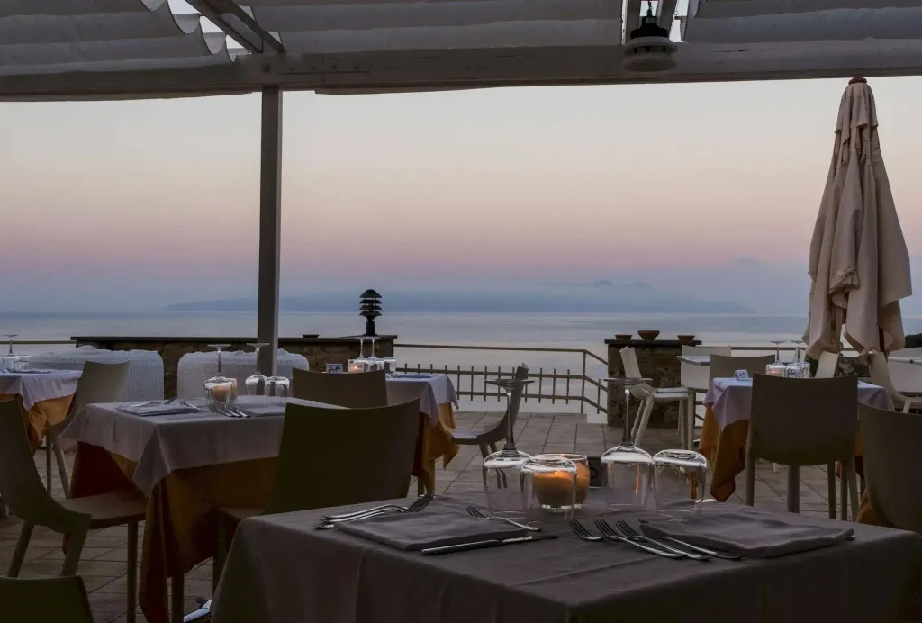 Tables dressées en extérieur avec vue sur la mer au coucher du soleil.