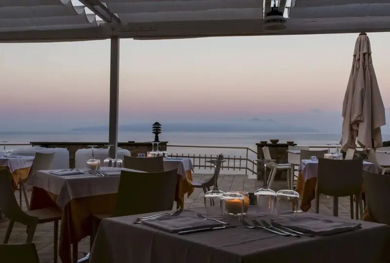 Tables dressées en extérieur avec vue sur la mer au coucher du soleil.