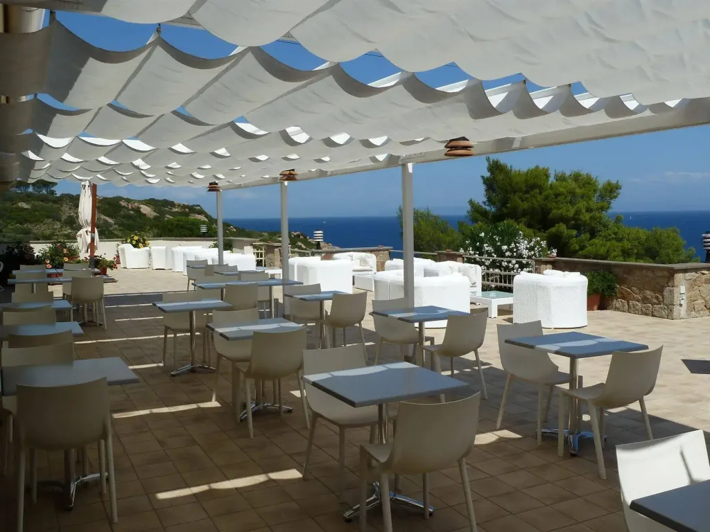 Terrasse ombragée avec tables et chaises donnant sur la mer.