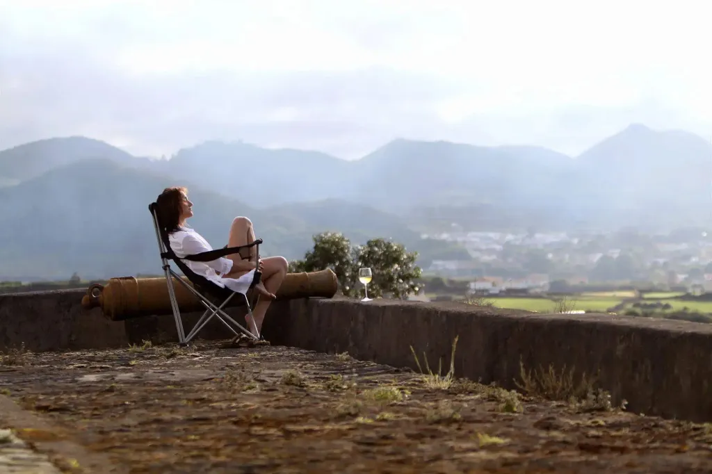 Une femme se détend sur une chaise longue face à un paysage montagneux.
