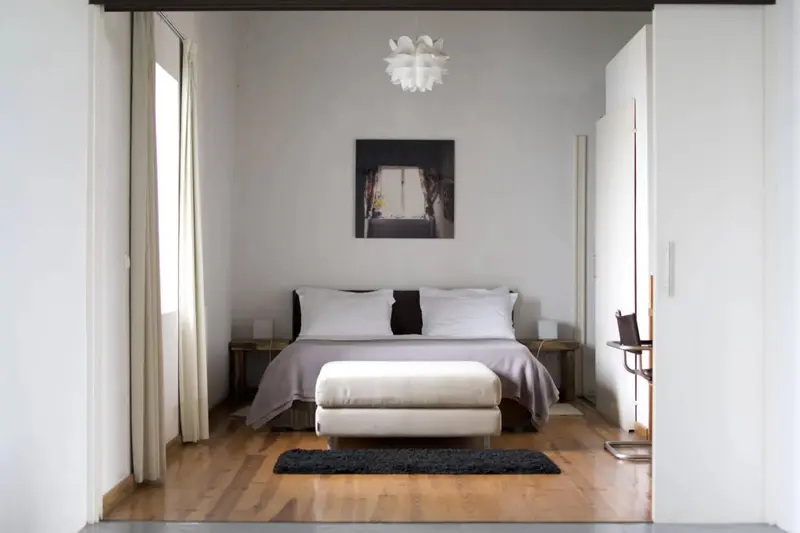 Une chambre lumineuse avec un grand lit et un banc au pied.