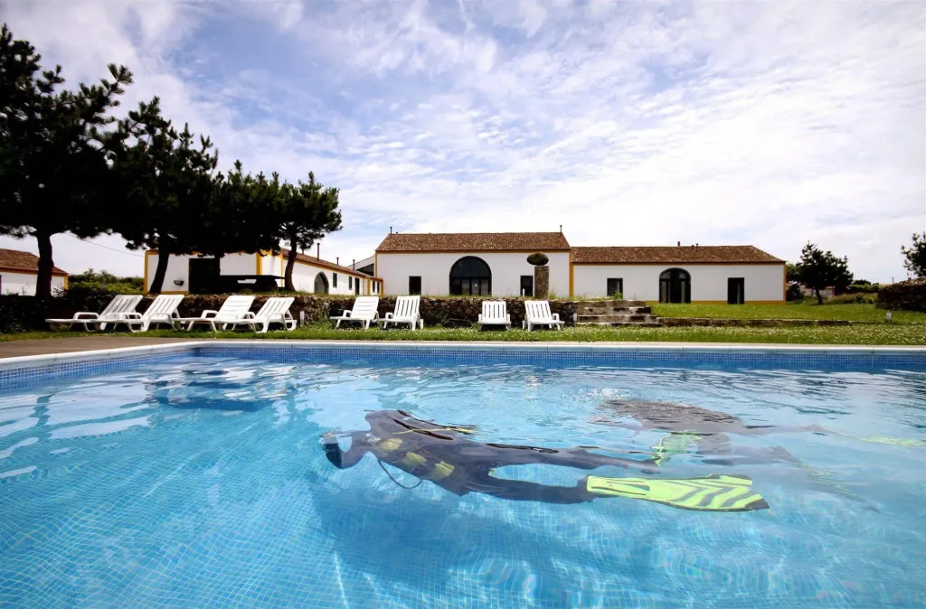 Une personne équipée nage sous l'eau dans une piscine devant un bâtiment blanc.