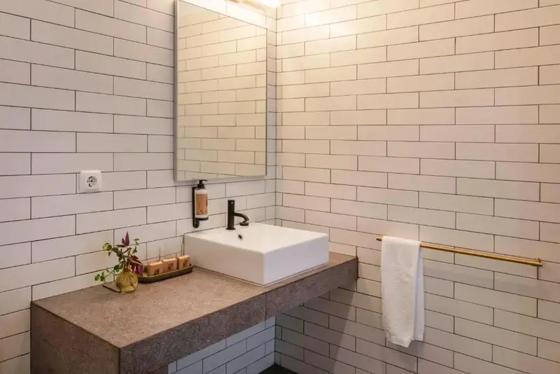 Un lavabo blanc est posé sur un meuble sombre dans une salle de bain carrelée.