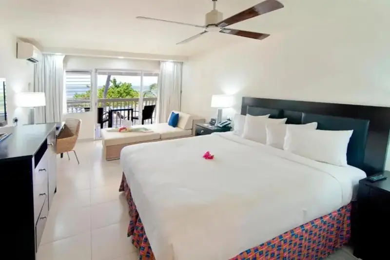 Une chambre lumineuse avec un grand lit et un coin salon donnant sur une terrasse.