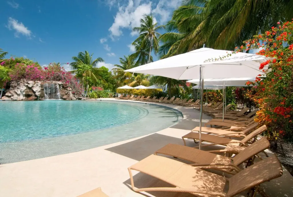 Transats blancs sous des parasols au bord d'une piscine turquoise.