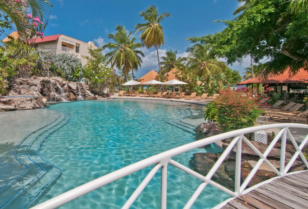 Une piscine turquoise avec une cascade artificielle et des transats sous des parasols.