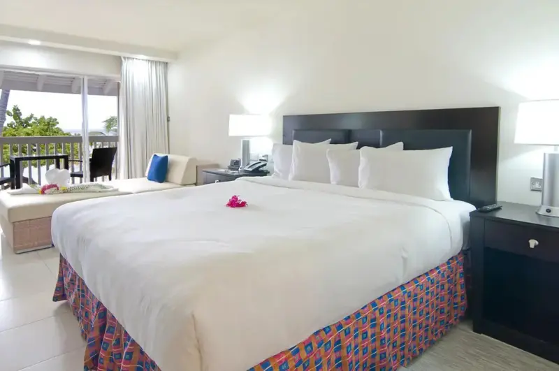 Une chambre lumineuse avec un grand lit recouvert de blanc et un coin salon.