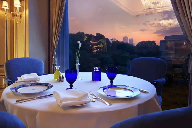 Table dressée dans une salle à manger élégante avec vue sur un paysage urbain au coucher du soleil.