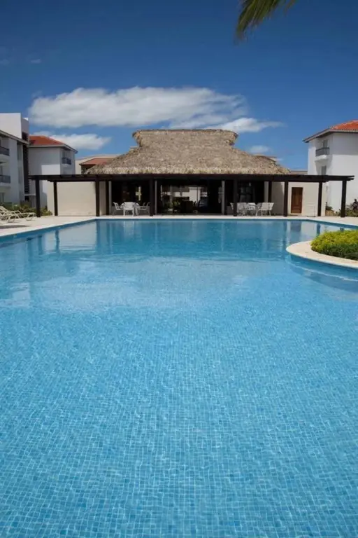 Une piscine rectangulaire turquoise invite à la détente sous un ciel bleu nuageux.