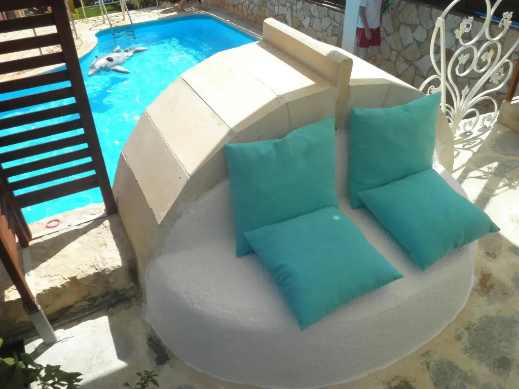 Espace de détente extérieur avec coussins turquoise près d'une piscine.