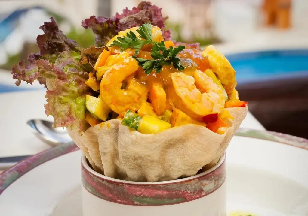 Une présentation de crevettes et de fruits frais est servie sur une assiette décorée.