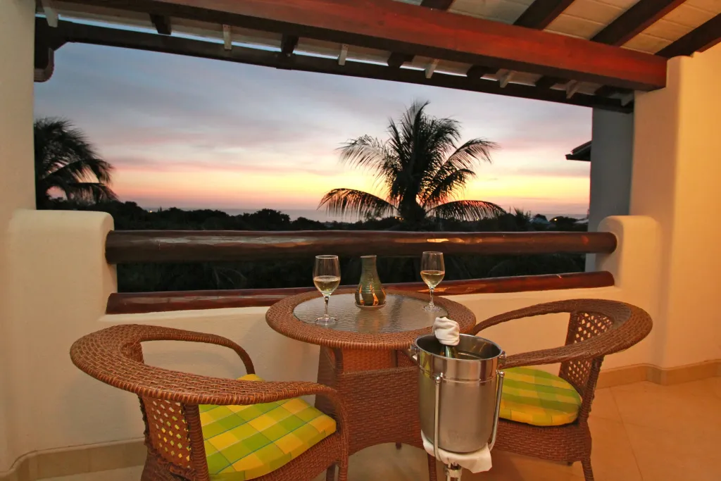 Une table ronde avec des verres et une bouteille est mise en valeur sur une terrasse avec vue sur un coucher de soleil tropical.
